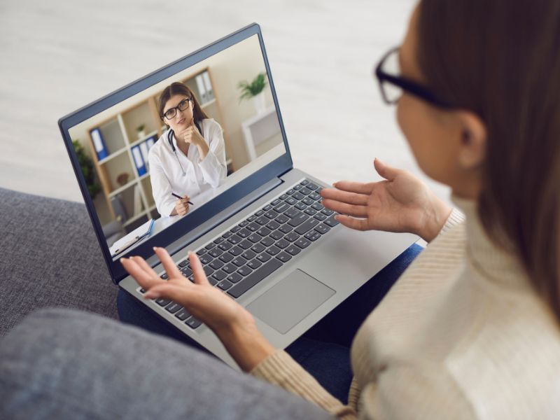 Młoda kobieta z laptopem i jej konsultacja online przed zabiegiem kosmetyczną z panią lekarz.